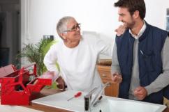 Plumbing contractor talks with customer while installing a new kitchen sink